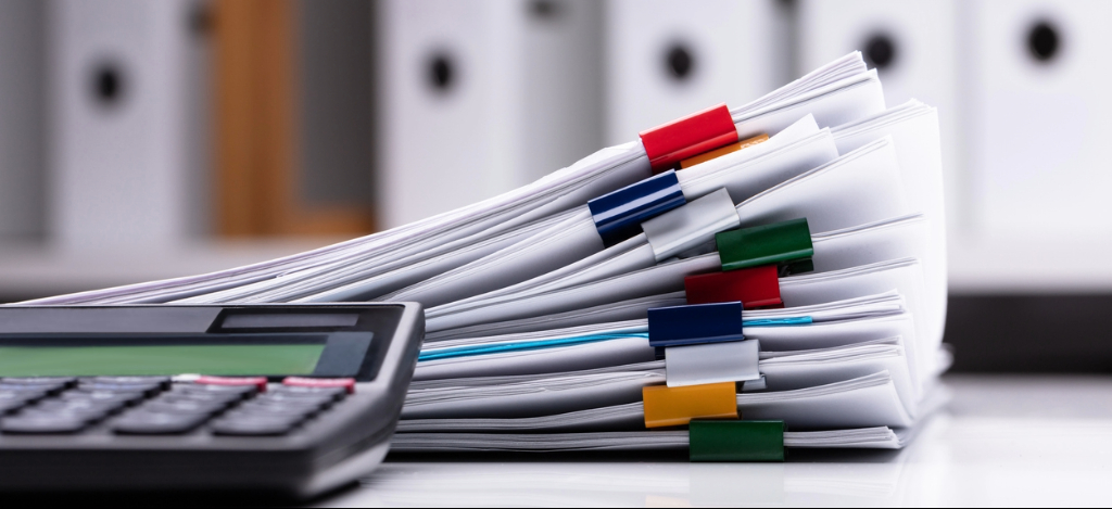 Dialysis Billing Challenges: A stack of paper documents and beside a calculator on a desk.