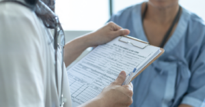 Preventing medical billing errors - Male doctor filling out a patient’s information form on a clipboard.