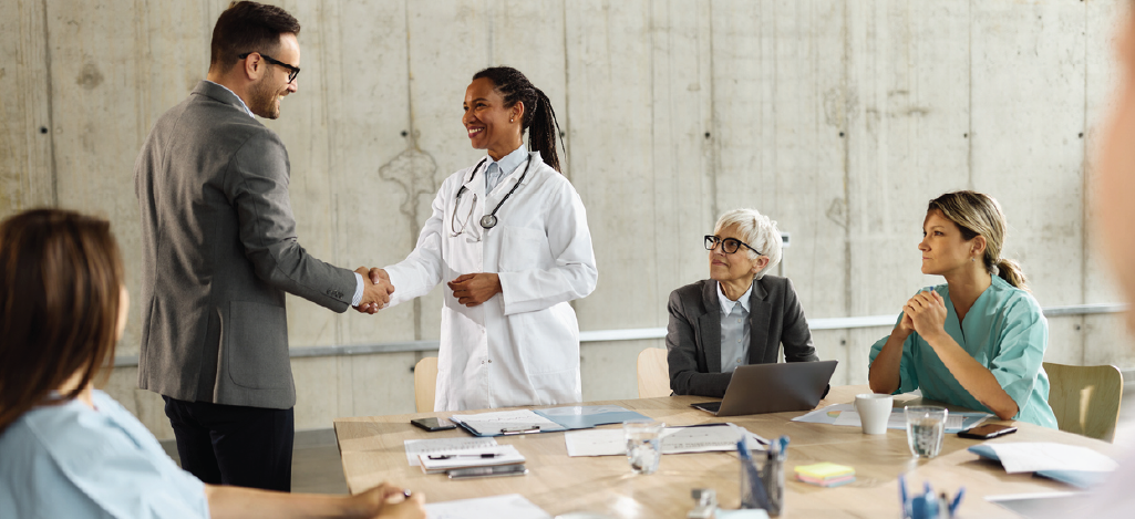 A female doctor shaking hands with a healthcare finance professional during a meeting.