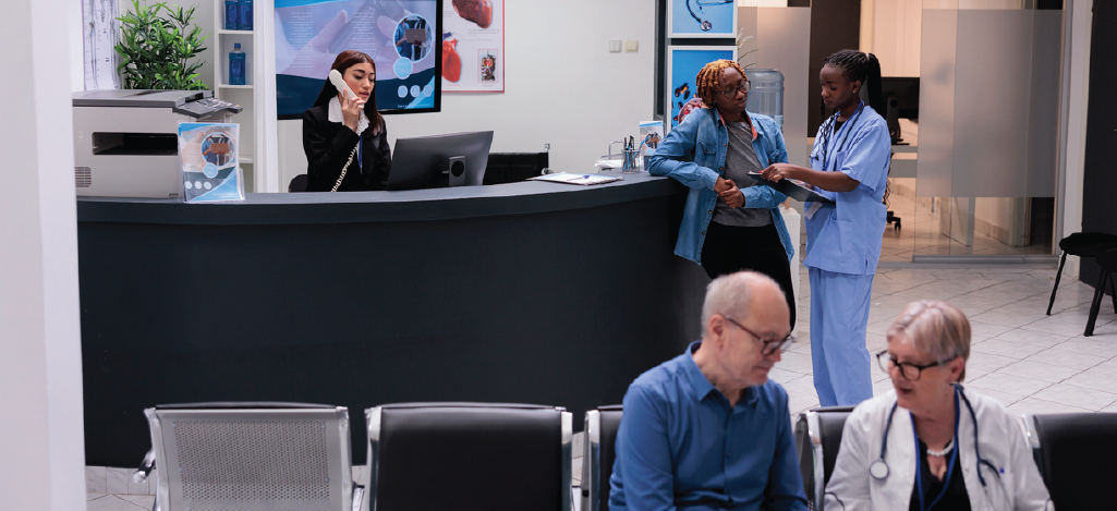 Nurse consulting patient at a clinic reception, doctor and patient talking while sitting down, receptionist at the phone.