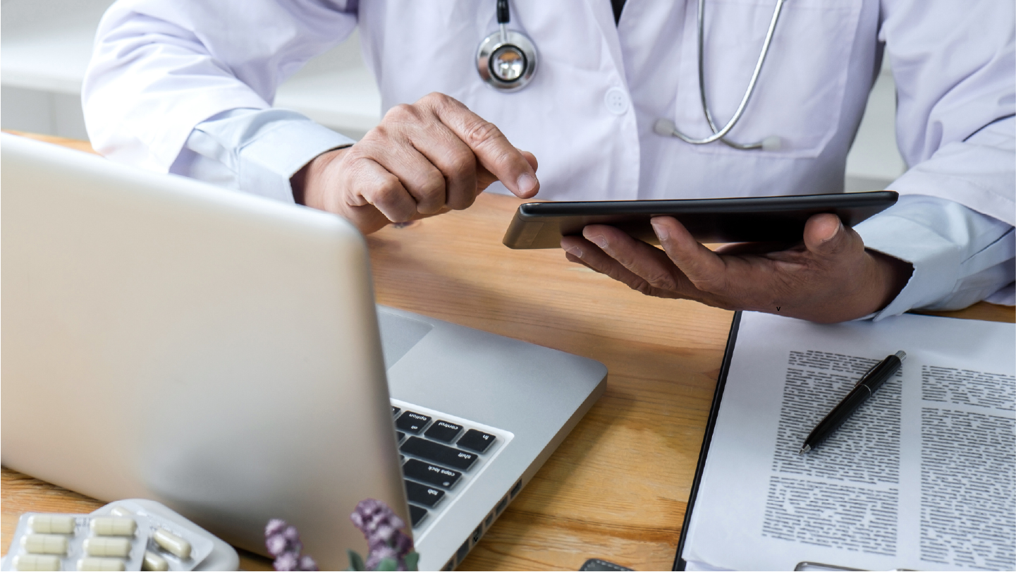 A doctor reviewing their revenue cycle management on a tablet and computer