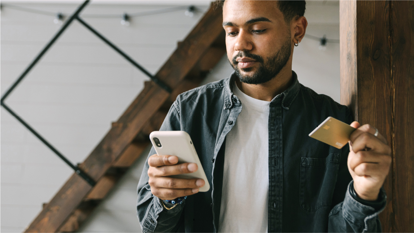 Man looking at his phone with his card in hand using healthcare payment solutions to pay a bill