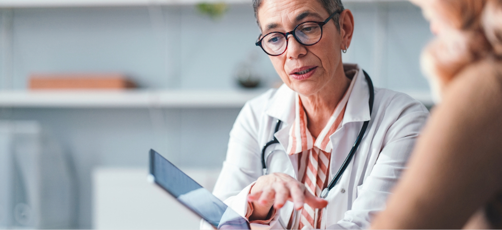 Rev cycle management - A female doctor holding a tablet device while explaining a patient’s medical bill.