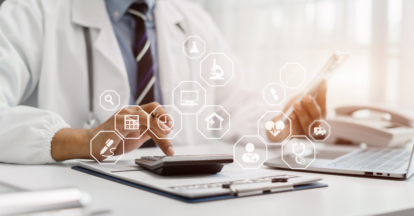 Healthcare payment trends - A male doctor using a calculator and a tablet device showing different medical technology icons.