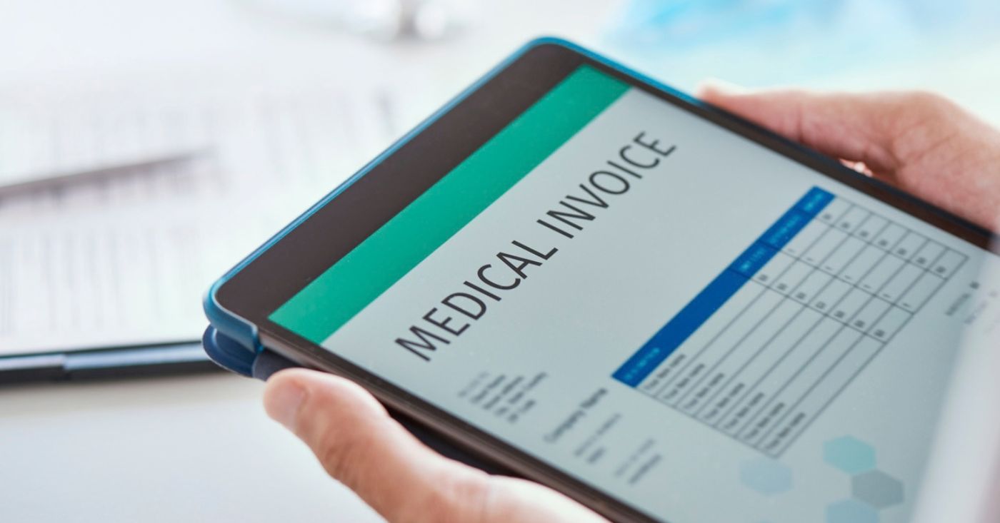 Closeup of hands holding a digital tablet with a medical invoice on screen.