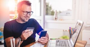 Combining mailed and eBills - A man at home using his smartphone and credit card to pay his medical bill.