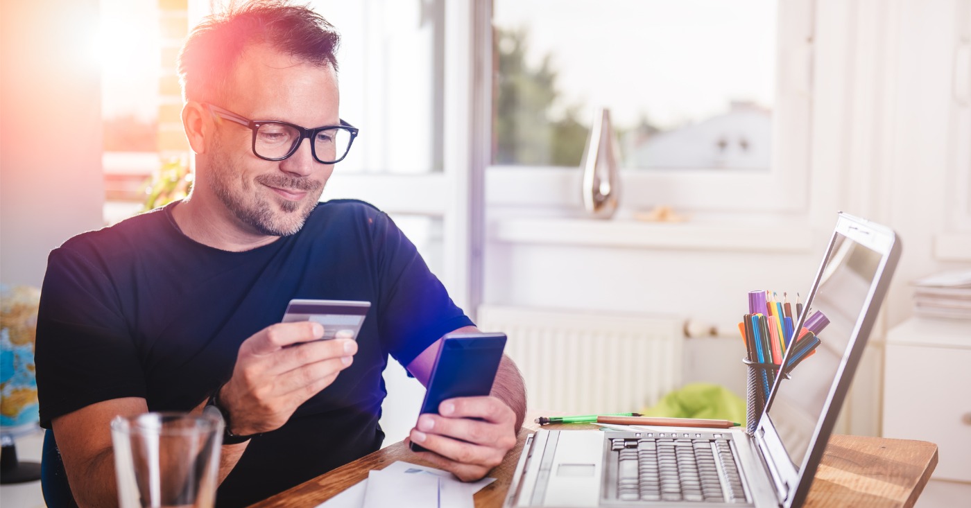 Combining mailed and eBills - A man at home using his smartphone and credit card to pay his medical bill.