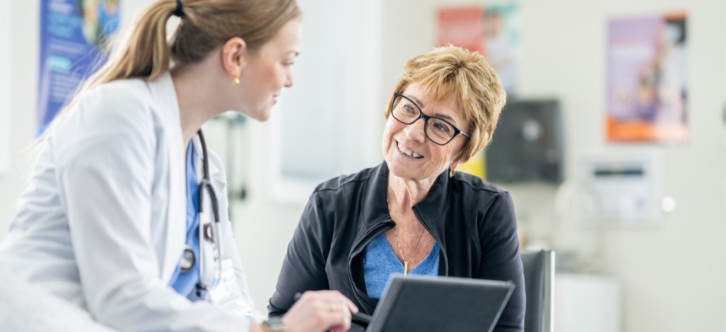 Enhancing patient journey - A female doctor holding a tablet device while discussing payment and treatment options with her senior patient.