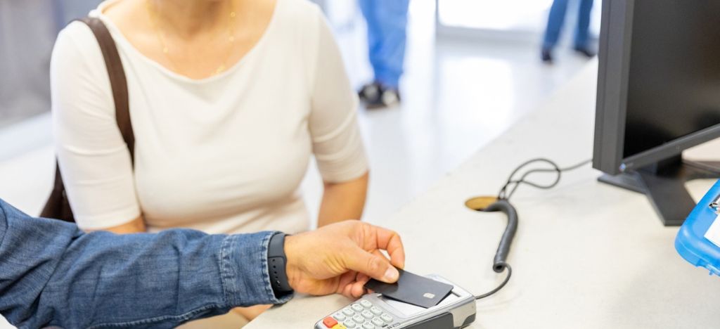 Cropped image of patient and companion tapping their card on a payment terminal at a healthcare practice.