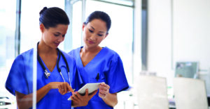 Using medical billing software for workflow automation - Two female medical professionals reviewing patients’ medical bills using a tablet device.