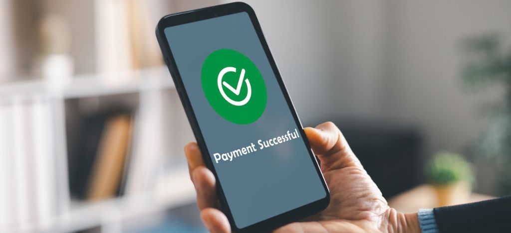 Cropped image of a smartphone in hand shows payment successful check mark.