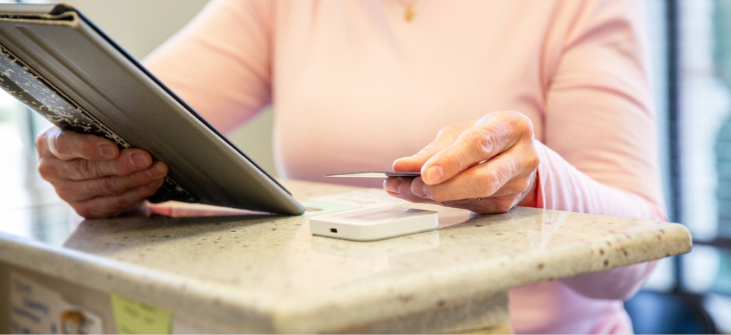 A senior woman holding a tablet device and a credit card while paying for her medical bill.