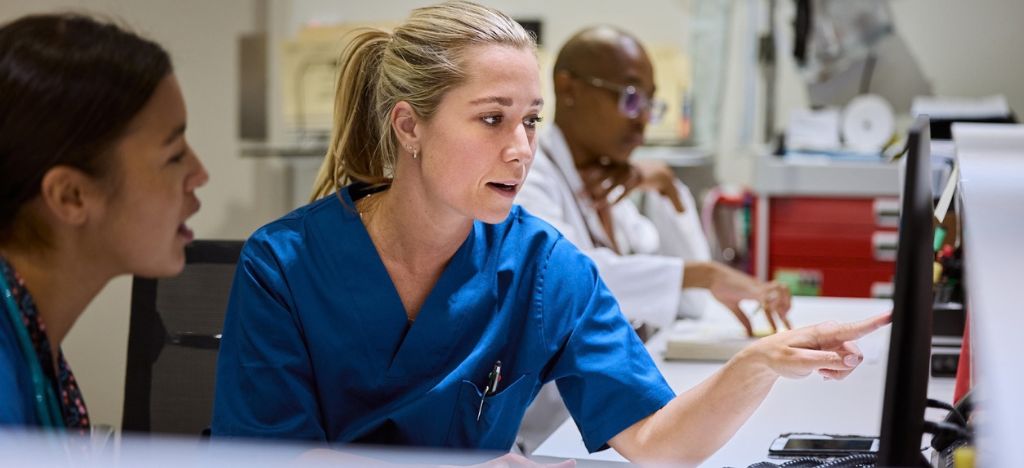 Healthcare team members discussing data on a desktop screen.