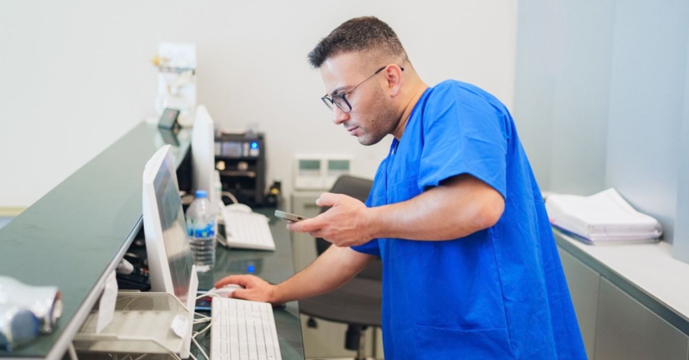 Healthcare staff using a mobile phone and the reception desktop pc.