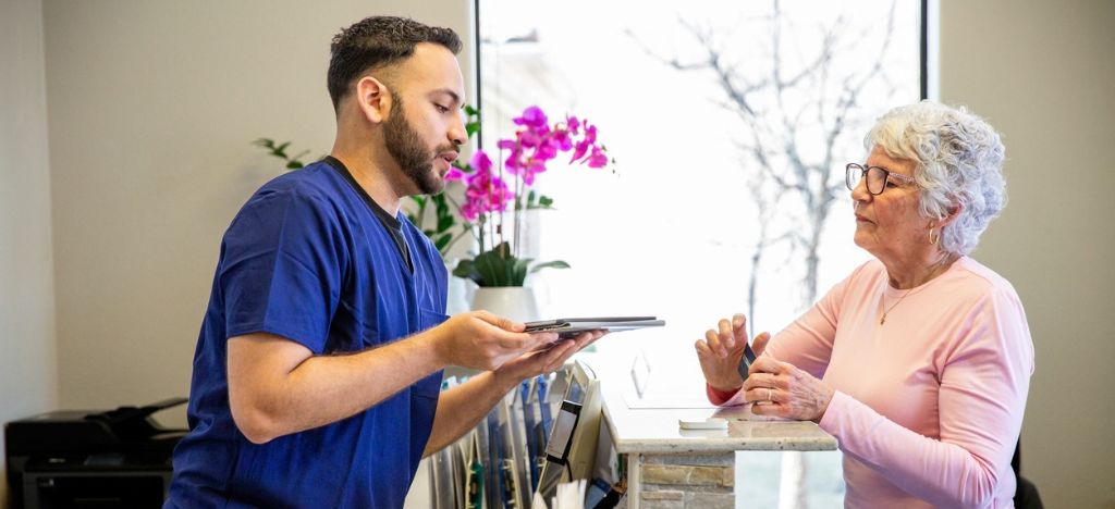 Healthcare practice staff talking to a senior lady at reception, hands over a clipboard.