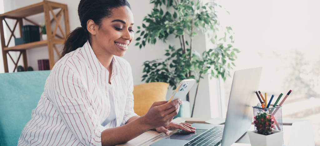 A woman using her smartphone and laptop to access her online medical bill.