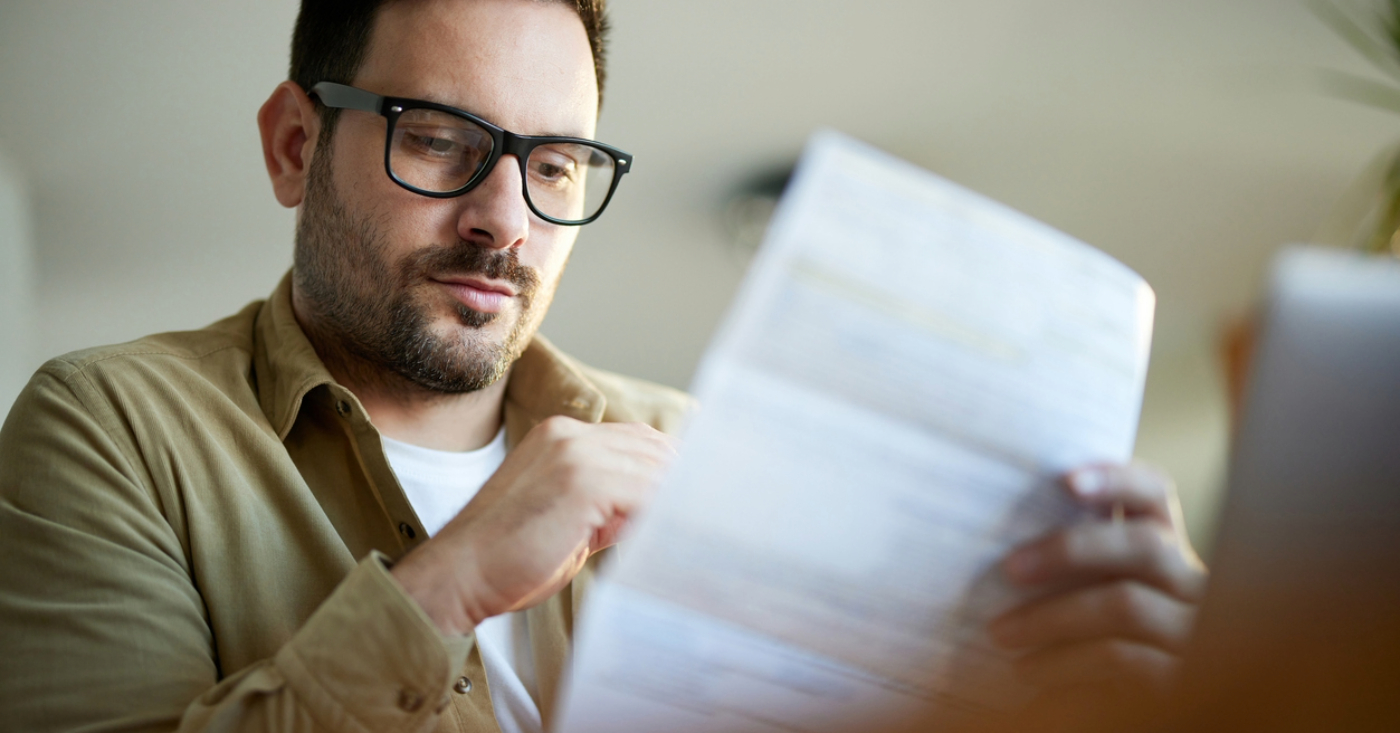 High-deductible health plans - A man at home reviewing his printed medical bill.