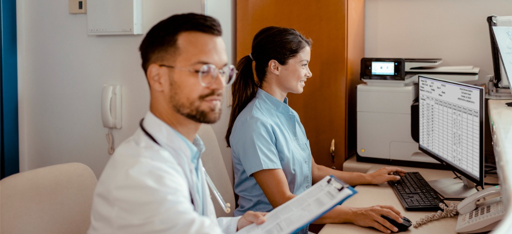 Improving healthcare revenue cycle - Two medical professionals reviewing patients’ medical bills using computers.