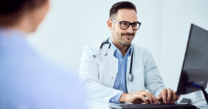 Patient communication platforms - A male doctor using a computer to check a patient’s medical charges.