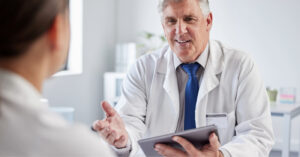 Patient billing support for healthcare providers - A doctor holding a tablet device while talking to his female patient during a medical appointment.