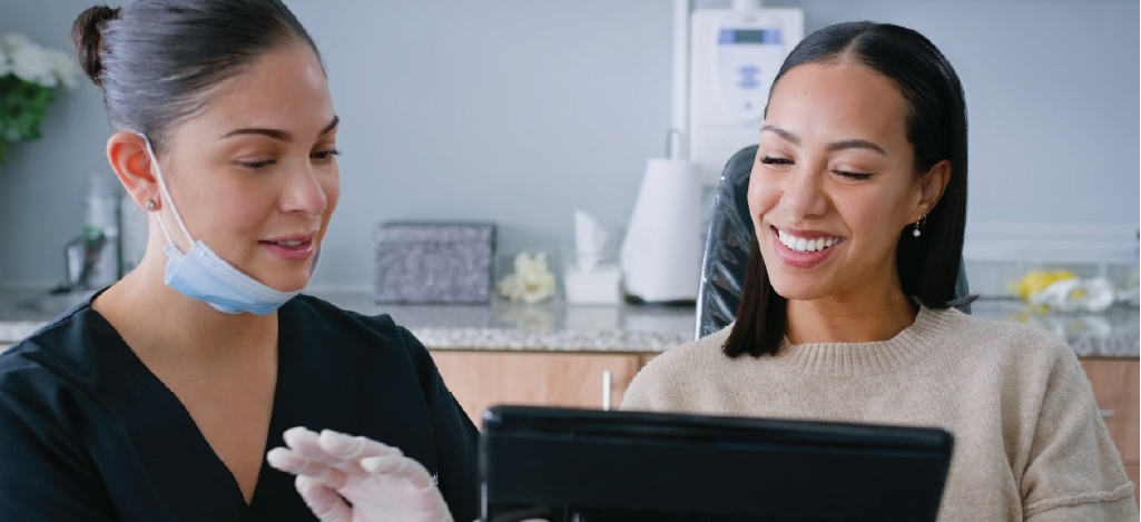 Using dental billing software - A female dentist using a tablet device to explain dental procedures to a female patient.