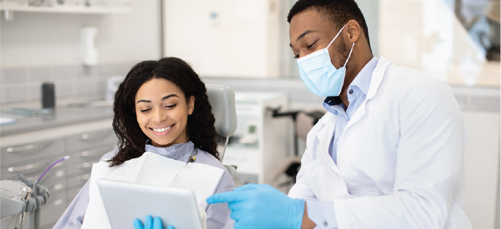 Choosing the right dental billing software - A male dentist using a tablet device while assisting a female patient.