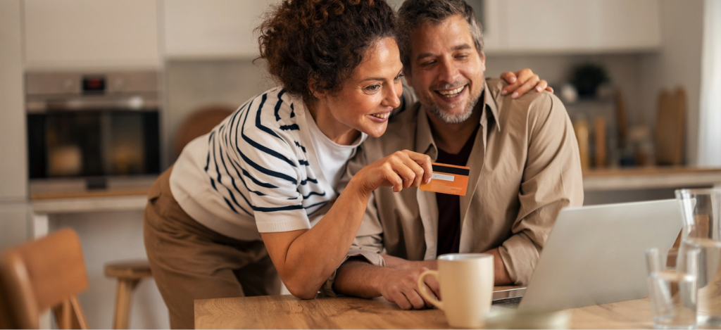RCM outsourcing companies - A mature couple at home using a laptop and a credit card to pay their medical bills online.
