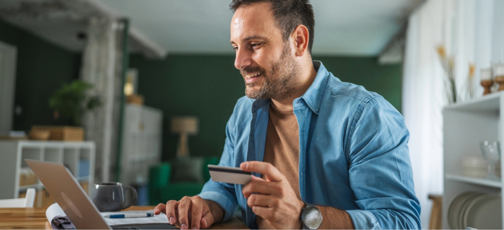 Patient messaging - A man at home holding his credit card while using his laptop to pay for his medical bill online.