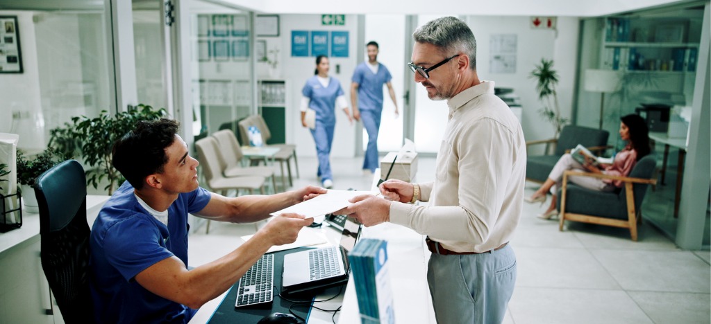 Understanding the patient roadmap - A male hospital staff member helping a man schedule his medical appointment.