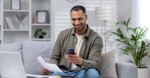 Leveraging automated payment reminders - A man at home using his smartphone to pay his medical bills.