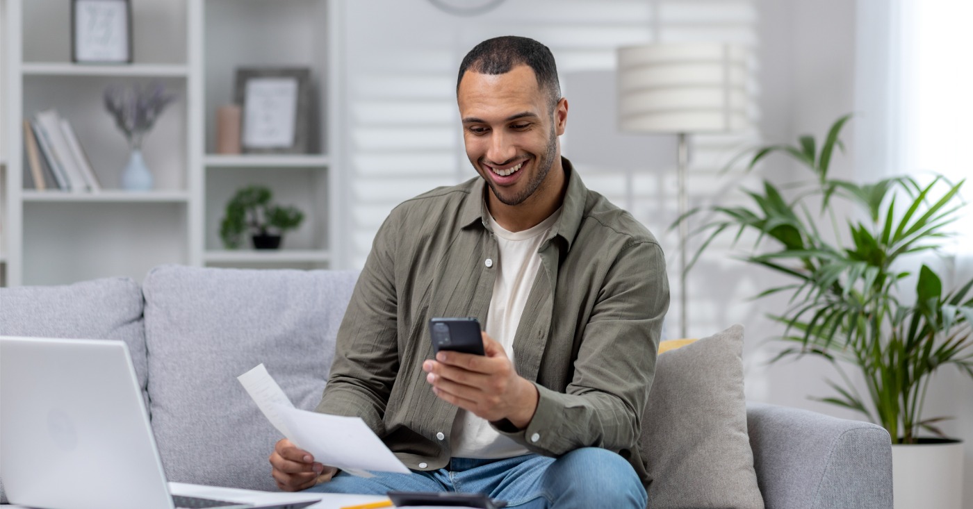 Leveraging automated payment reminders - A man at home using his smartphone to pay his medical bills.