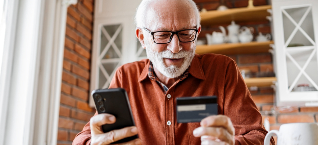 Healthcare RCM companies - A senior man at home paying his online medical bill using his smartphone and credit card.