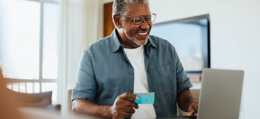 Get paid faster - A senior man at home using his laptop and credit card to pay for his medical bill.