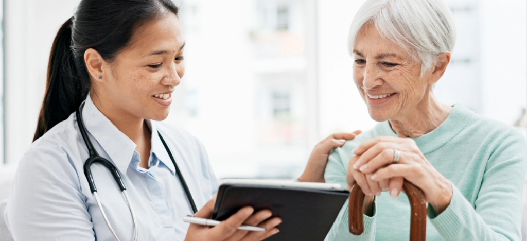 A female doctor holding a tablet device while explaining patient financing to her senior patient.