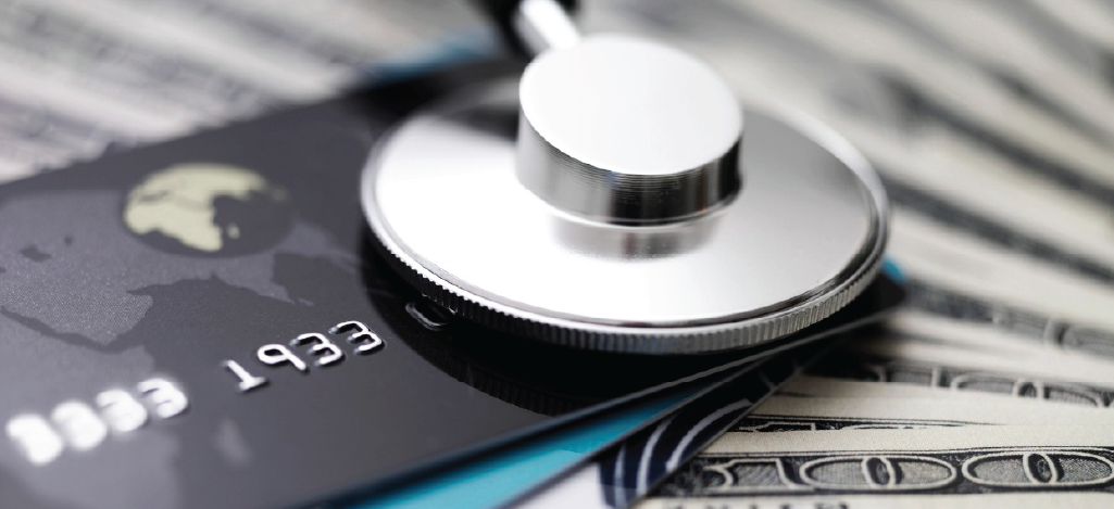 Medical credit card processing - Several dollar bills, credit cards, and a doctor’s stethoscope on top of a table.