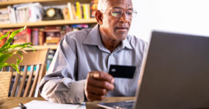 Types of payment methods - A senior man at home using his credit card and laptop to pay for his medical bill online.