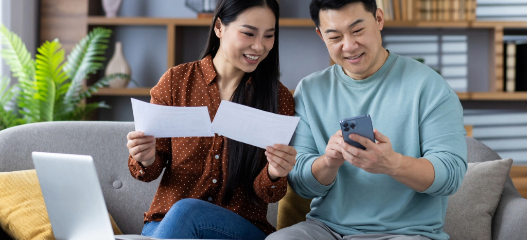 Navigating deductible reset - A couple at home using a smartphone and a laptop to enroll for a flexible payment option.