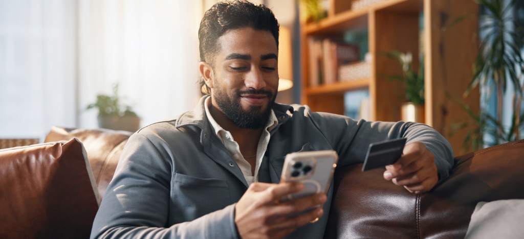 RCM company - A man at home paying his medical bill online using his smartphone and credit card.
