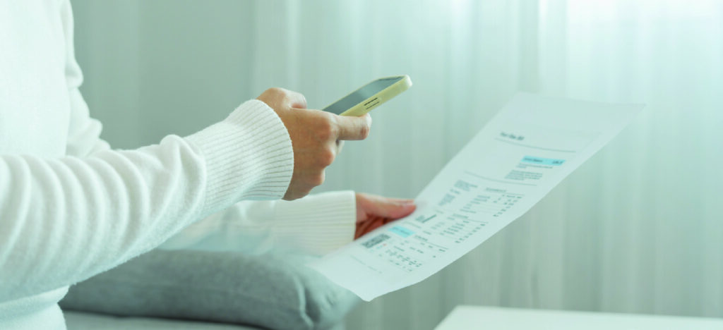 Improving patient communication through billing - A woman at home using a smartphone to scan a QR code printed on her medical bill.