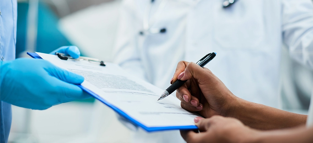 Female patient signing medical insurance form in front of her doctors.
