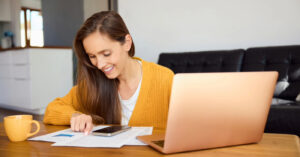Patient payment solutions - A woman at home using her laptop and smartphone while reviewing her printed medical bill.