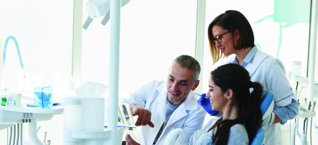 Breaking down costs for patients who can’t afford dental care - A male dentist and his assistant explaining a dental procedure to a female patient.