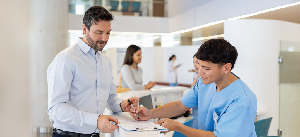 Patient financing benefits - A male medical staff assisting a male patient in signing a medical document.