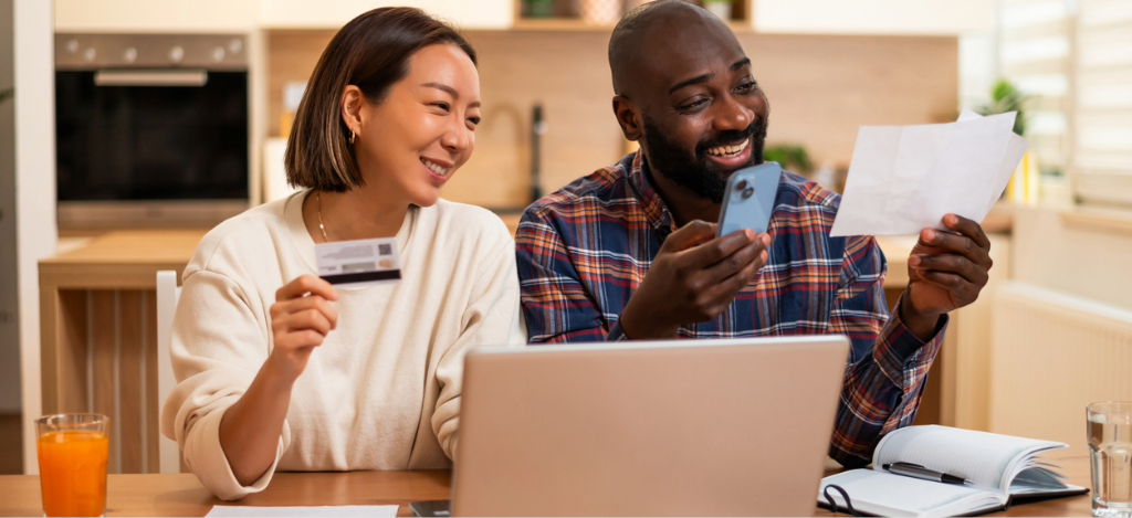 Patient payment solutions - A couple at home using their credit card, smartphone, and laptop to pay for their medical bills online.