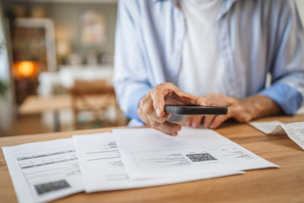 Adopting rising healthcare payment trends - A man using a smartphone to scan a QR code printed on his medical bill.