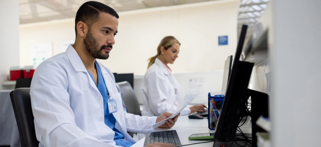 Get paid faster - Two doctors at a hospital billing desk using computers to review patients’ medical bills.