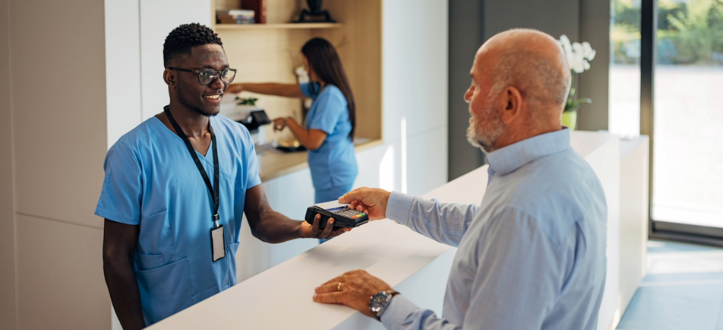 Medical billing issues - A male hospital staff member assisting a male senior patient in paying his medical bill.