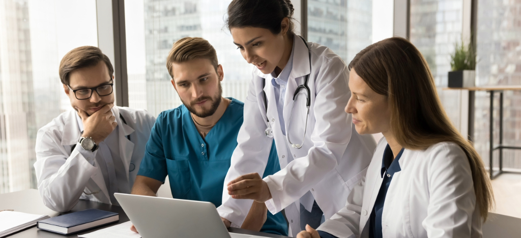 Get paid faster - A team of medical professionals using a laptop while discussing their revenue cycle.