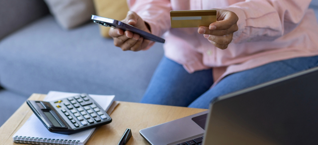 Self-payment solutions for patients - A woman at home holding a smartphone and a credit card while paying for her medical bills.