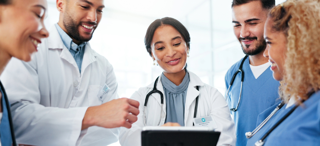 Using automatic payment programs - A team of doctors looking at a tablet device while discussing their practice’s revenue.